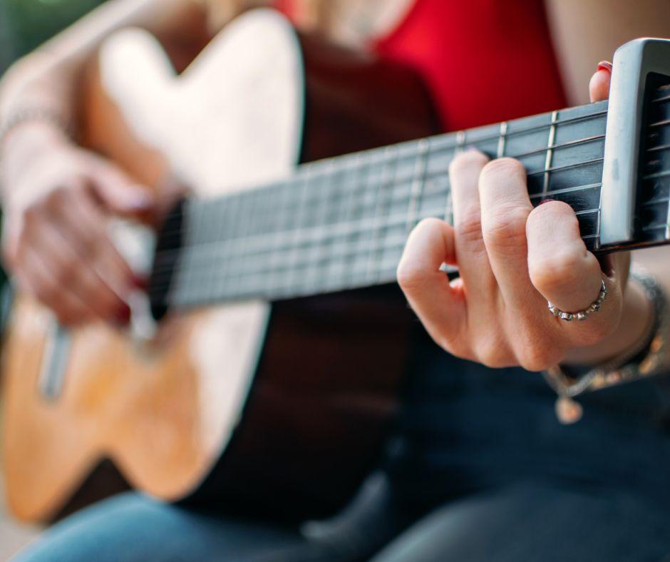 close up of a person's left hand on the fretboard of an acoustic guitar