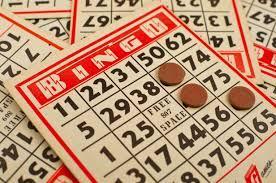 A pile of tan and red bingo cards. The one on the top of the pile has three tan markers on it.