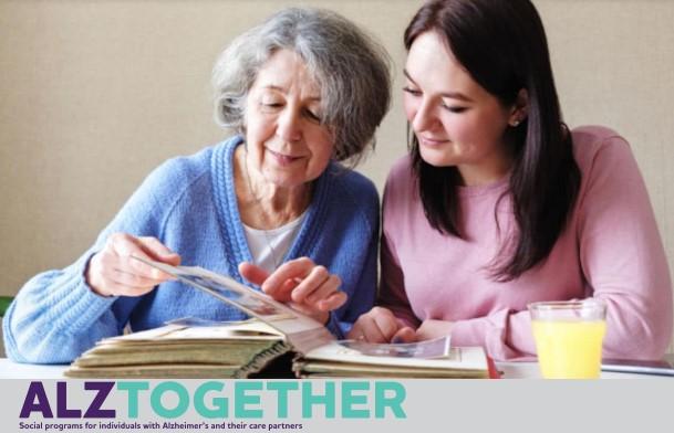 an older woman with grey hair and a younger woman with brown hair are looking at a photo album together.